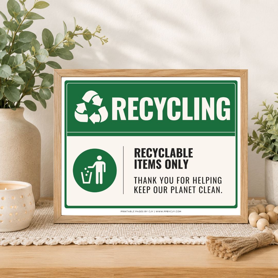 A framed recycling sign displayed on a wooden table in a styled home setting with plants, a candle, and decorative beads. The sign features a green and white design with the text 'RECYCLING' and 'RECYCLABLE ITEMS ONLY'.