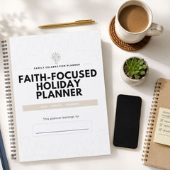 A spiral-bound 'Faith-Focused Holiday Planner' notebook is shown in a styled flat-lay arrangement on a white surface, surrounded by a cup of coffee, a small succulent, a smartphone, and other notebooks.
