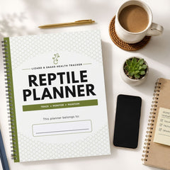 A spiral-bound notebook titled 'REPTILE PLANNER' is shown in a styled flat-lay arrangement on a white surface, alongside a cup of coffee, a pen, a small succulent, a smartphone, and another notebook.