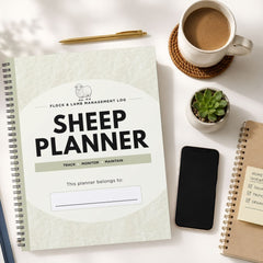 A spiral-bound 'Sheep Planner' from Flock & Lambs Management Log is displayed in a styled flat-lay arrangement on a white surface, surrounded by a cup of coffee, a pen, a small succulent, a smartphone, and another notebook.