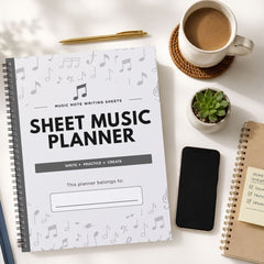 A spiral-bound sheet music planner notebook with a white cover printed with black musical notes and the title 'SHEET MUSIC PLANNER' is shown in a styled flat-lay on a white surface, alongside a pen, coffee cup, small plant, smartphone, and another notebook.