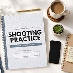 A spiral-bound notebook titled 'SHOOTING PRACTICE' lies on a white tabletop, surrounded by a cup of coffee, a pen, a small succulent, a smartphone, and another notebook.