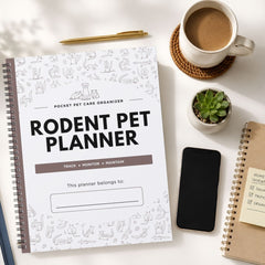 A spiral-bound 'Rodent Pet Planner' notebook is shown in a styled flat-lay arrangement on a white surface, surrounded by a cup of coffee, a small succulent, a smartphone, and another notebook.