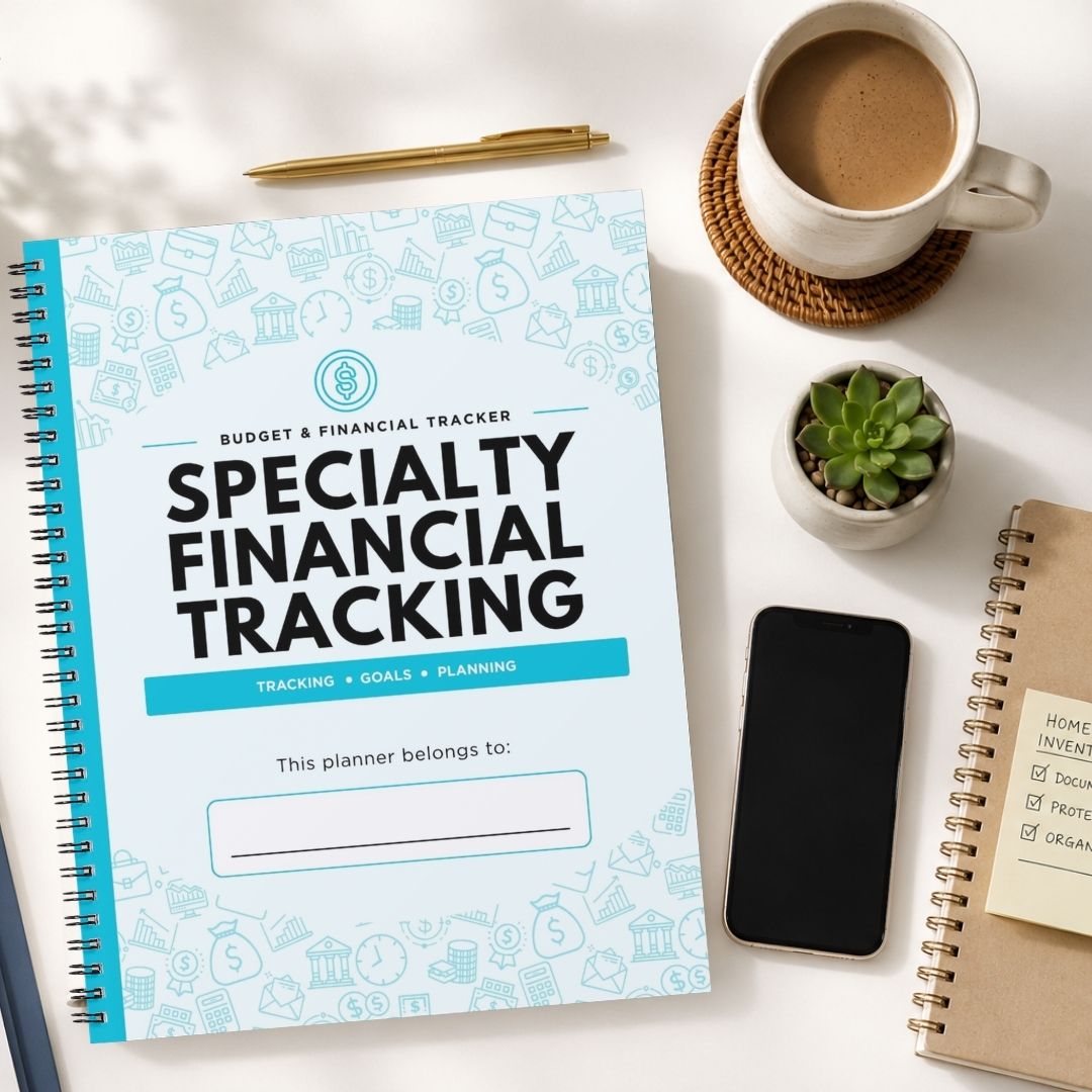 A spiral-bound planner titled 'Specialty Financial Tracking' lies on a white desk surrounded by a coffee cup, a small succulent, a smartphone, and other notebooks.