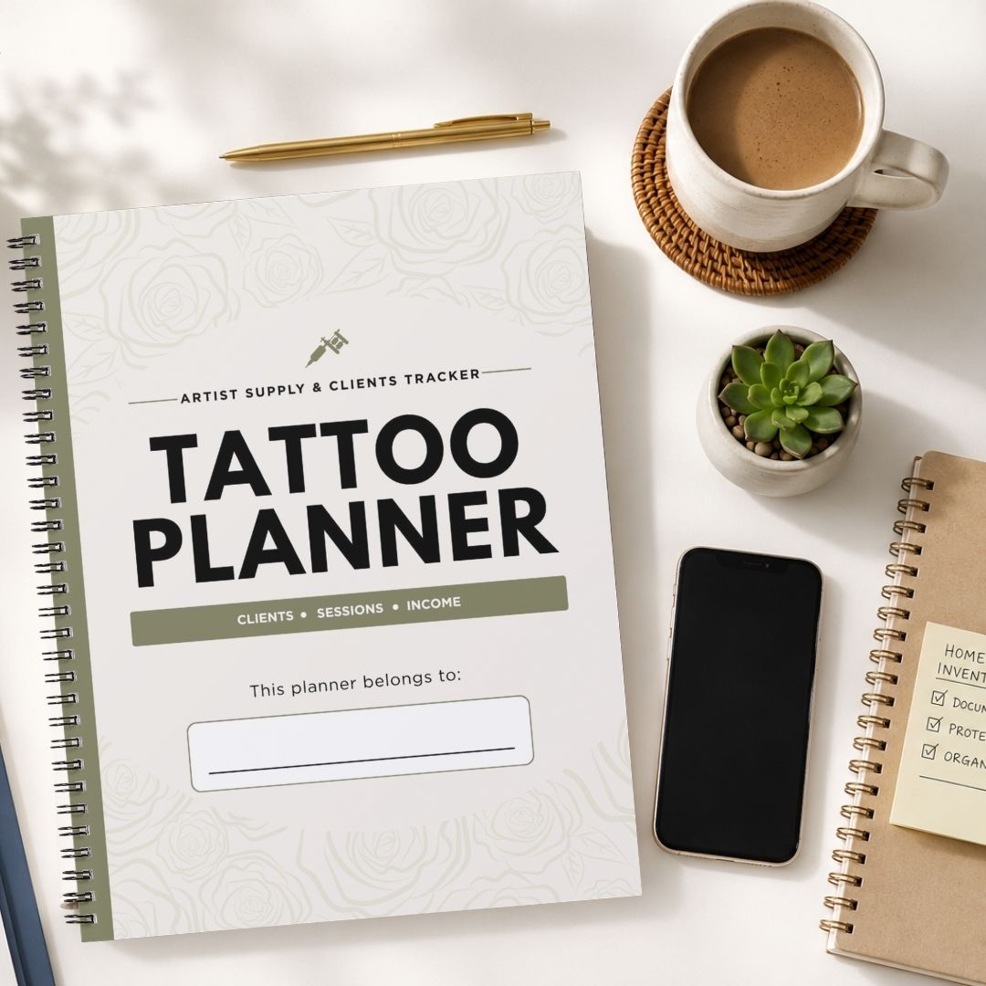 A spiral-bound 'Tattoo Planner' notebook is shown in a styled flat-lay arrangement on a white surface, alongside a cup of coffee, a pen, a small succulent, a smartphone, and another notebook.