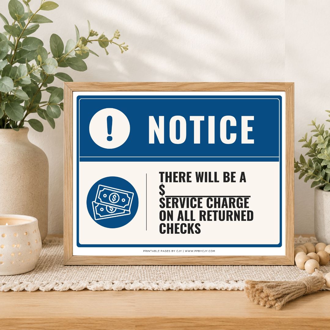 A framed printed notice sign on a tabletop in a styled interior setting. The sign has a blue border, a blue header with a white exclamation mark and the word NOTICE, and black text stating there will be a service charge on all returned checks.