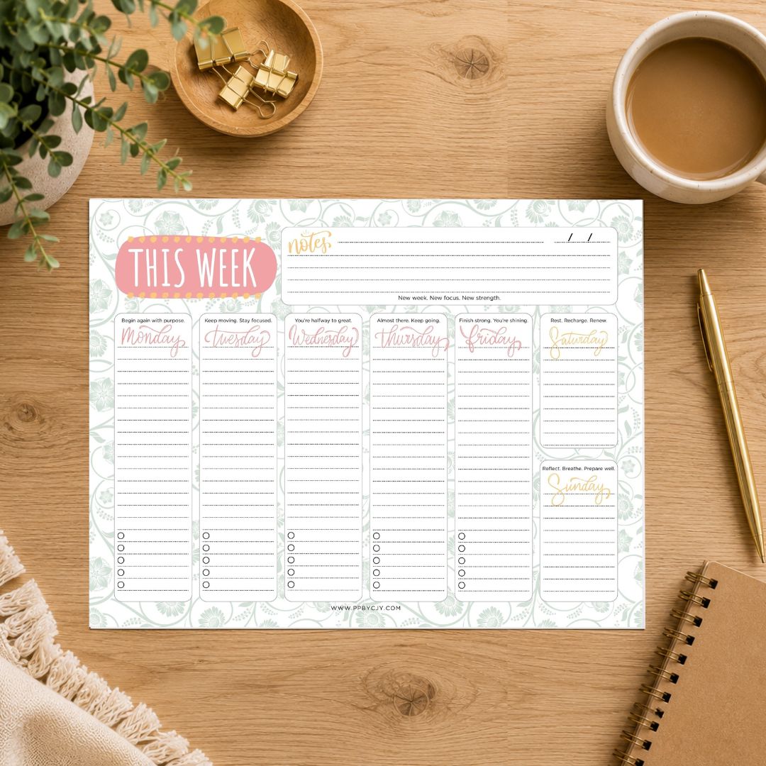 A weekly planner notepad sheet laid flat on a wooden desk, surrounded by a coffee cup, plant, binder clips, pen, and notebook. The planner has a pale floral border and sections labeled Monday through Sunday, with a pink title bubble reading THIS WEEK.
