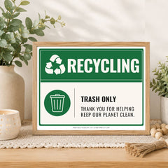 A framed recycling sign displayed on a wooden table in a styled home setting. The sign features a green and white design with the text 'RECYCLING' and 'TRASH ONLY THANK YOU FOR HELPING KEEP OUR PLANET CLEAN.