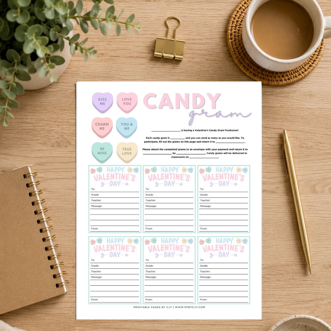 A Valentine's Day printable card set titled 'Candy from' laid flat on a wooden desk, surrounded by a coffee cup, binder clip, plant, notebook, and pen.