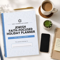A spiral-bound 'Family Celebration Planner' titled 'Jewish Faith-Focused Holiday Planner' is displayed in a styled flat-lay arrangement on a white surface alongside a coffee cup, a pen, a small succulent, a smartphone, and another notebook.