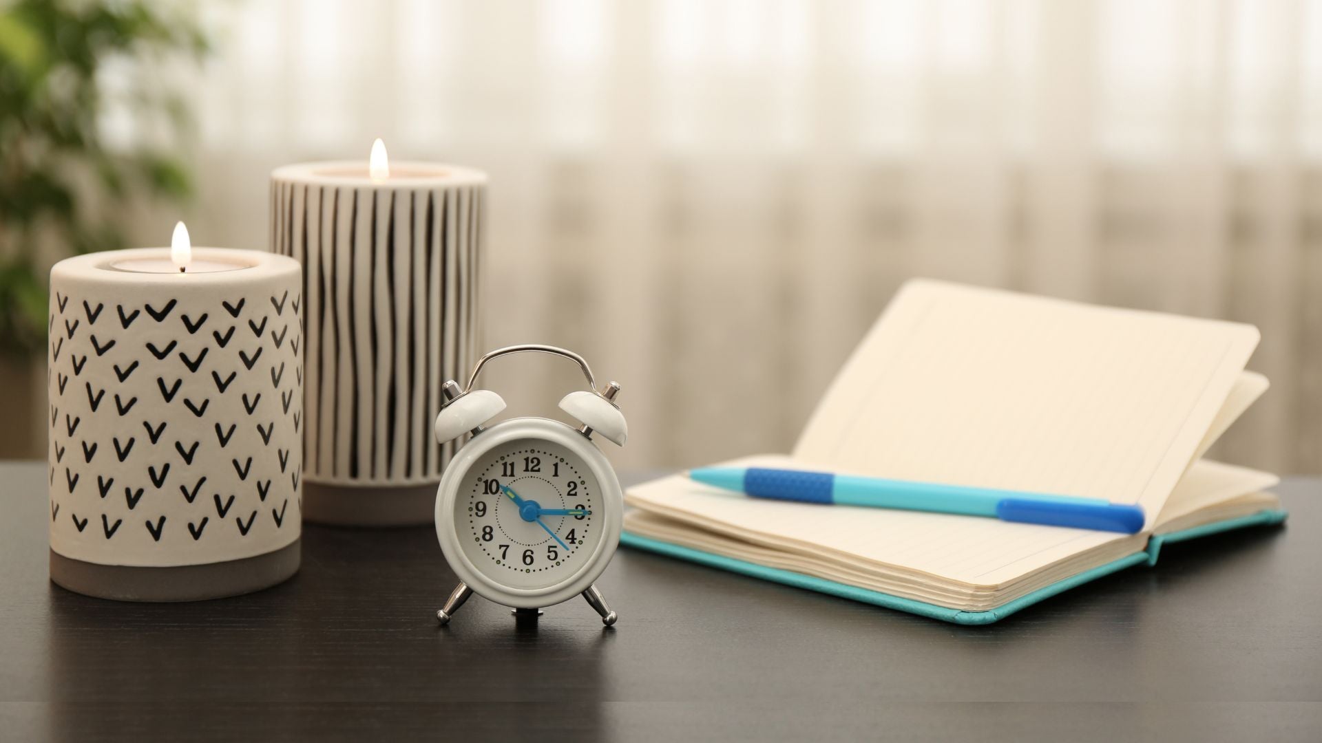 Candles, alarm clock, and notebook on a table with a blurred background