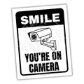 Sign with a camera illustration and text 'SMILE YOU'RE ON CAMERA' on a white background